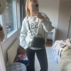 Svart axelväska i syntet - Snygg svart axelväska i syntet med krokodilpräglat mönster. Väskan har en justerbar axelrem och stängs med en tryckknapp. Perfekt för att bära dina nödvändigheter med stil. Från Åhléns 