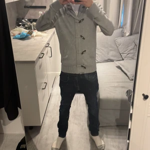 Tröja/cardigan - Säljer en stilren grå hoodie med knappar framtill. Tröjan har långa ärmar och ribbade muddar vid ärmslut och nederkant. Perfekt för kyligare dagar.