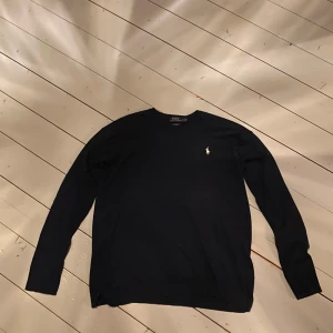 Svart tröja från Ralph Lauren - Snygg svart tröja från Ralph Lauren med lång ärm och klassisk design. Den har en liten broderad logga på bröstet i gult. Perfekt för en stilren look.