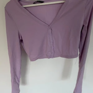 Ljuslila croppad kofta från SHEIN - Säljer en superfin ljuslila croppad kofta från SHEIN. Den har långa ärmar och knappar framtill, perfekt för vår och sommar. Materialet är mjukt och bekvämt, vilket gör den idealisk för både vardag och fest. Passar perfekt till ett par höga jeans eller en söt kjol!