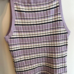 Lila randig ribbad topp - Säljer en superfin lila ribbad topp med svarta och vita ränder. Den är ärmlös och perfekt för sommardagar. Toppen har en skön passform och är gjord i ett mjukt material.