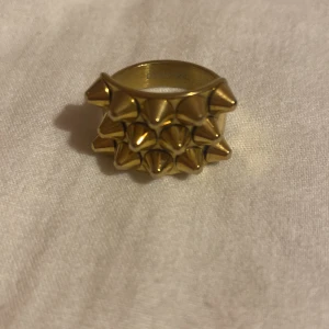 Guldfärgad ring med nitar från Edblad - Säljer en guldfärgad ring från Edblad. Ringen har ett unikt design med flera små nitar som ger den en edgy look. Perfekt för att ge din outfit lite extra attityd! Kommer i originalförpackning.(Stockholmsstil)