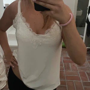 Vit linne med spetsdetaljer - Säljer ett superfint vitt linne med spetsdetaljer runt halsringningen. Perfekt för sommardagar eller som ett lager under en kavaj. Linnet är ärmlöst och har en lös passform som gör det bekvämt att bära.