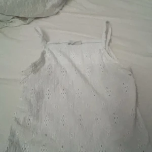 Vit ärmlös topp från Kappahl - Säljer en söt vit ärmlös topp från Kappahl. Den har ett fint broderat mönster och smala axelband. Perfekt för sommardagar eller som ett lager under en kofta. Toppen är i bra skick och redo för en ny ägare! Den är egentligen en volangtopp men jag har klippt i ärmarna så det blev ett linne men det är inget som man tänker på, även ett litet hål vid ena ärmen men det är inte heller något man tänker på.