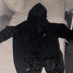 Svart jacka från Haglöfs - Säljer en svart jacka från Haglöfs med huva och dragkedja. Jackan har en quiltad design och är perfekt för kyligare väder. Den är långärmad och har en stilren look.