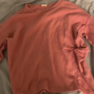 Rosa rosett tröja (barn) - Mysig rosa tröja med lång ärm och en enkel design. Perfekt för kyligare dagar med sin bekväma passform och mjuka material.