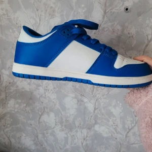 Blå och vita sneakers - Snygga sneakers i blått och vitt med snörning. Perfekta för en sportig look. Skorna har en klassisk design med perforerade detaljer på tån för extra ventilation.
