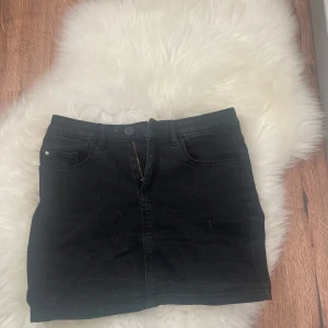 Svart jeanskjol - Snygg svart jeanskjol med klassisk femficksdesign och knappstängning fram. Perfekt för en stilren look.