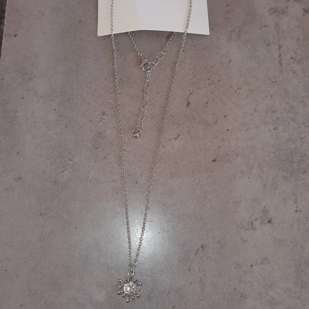 Elegant silverfärgat halsband med ett vackert hänge. Hänget har en glittrande sten i mitten som fångar ljuset fint. Perfekt för att ge en vinterkänsla till din outfit.. Asusteet.