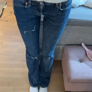 Blå jeans med slitningar - Snygga blå jeans med slitningar på knäna. De har en klassisk femficksdesign och en lågmidjad passform. Perfekta för en avslappnad stil.