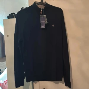 Svart tröja med dragkedja från Morris - Snygg svart tröja från Morris med dragkedja vid halsen och ett diskret broderat märke på bröstet. Perfekt för en stilren look. Tröjan har långa ärmar och en klassisk passform. Strl M men passar perfekt på s som på bild. Endast en gång använd så lapparna borta