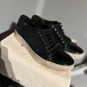 Svarta skor från Lanvin captoe - Snygga svarta sneakers från Lanvin med snörning och vit sula. Skorna har en stilren design med en blank tå och är perfekta för en avslappnad look. Passar bra till jeans och andra casual outfits.