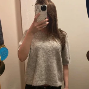 Grå ulltröja med korta ärmar - Mysig grå tröja i ull med korta ärmar. Perfekt för kyliga dagar när du vill ha något bekvämt och stilrent. Tröjan har en rund halsringning och en lös passform. Den är ifrån MQ och är i storlek S❤️ tröjan är andvänd få tal gånger 