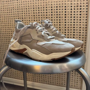 Beige sneakers från Timberland - Snygga beige sneakers från Timberland med vit sula och bruna detaljer. Skorna har snörning och en robust design som passar perfekt för vardagsbruk. Timberland-loggan syns på sidan och sulan.