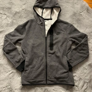 Grå fleecejacka från Nike - Säljer en grå fleecejacka från Nike med huva och dragkedja. Hoodien har en praktisk bröstficka . Den är långärmad och har en mjuk insida för extra komfort. Perfekt för dig som gillar en sportig stil! storlek (147-158)cm. nypris 1200 kr, pris kan diskuteras!