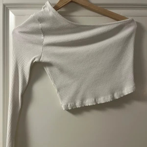 Vit ribbad oneshoulder topp - Säljer en stilren vit ribbad oneshoulder topp. Den har en lång ärm och är croppad. Den är från Nakd och storlek s. Aldrig använd. 