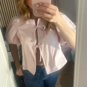 Ljusrosa blus med knytband - Söt ljusrosa blus med korta puffärmar och knytband framtill.