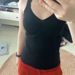 Svart ribbad linnetopp - Snygg svart ribbad linnetopp med smala axelband och v-ringning. Perfekt för en stilren look och kan enkelt matchas med olika outfits. Har ett stretchigt tyg med mönster i.