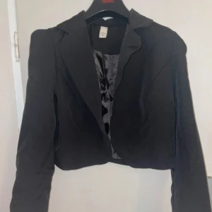 Svart kavaj med satin-foder - Snygg svart kavaj med ett elegant satin-foder. Kavajen har en klassisk design med långa ärmar och en stilren krage. Perfekt för att ge en sofistikerad touch till din outfit.