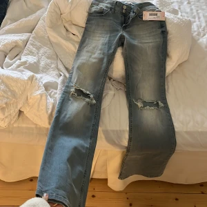 Ljusa jeans med slitningar från Nelly - Snygga ljusblå jeans från Nelly med slitningar på knäna. De har en låg midja och stängs med tre knappar. Baktill finns fickor med dekorativa knappar. Perfekta för en avslappnad stil. Köptes för 699, säljs för 499