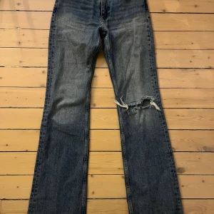 Blå jeans från Gina Tricot - Säljer ett par blå jeans från Gina Tricot. De är utsvängda  med en slitning på ena benet. Jeansen har en knapp och dragkedja framtill. De är medel höga i midjan. Använda fåtal gånger. Nypris 500 kr. Pris kan diskuteras!❤️