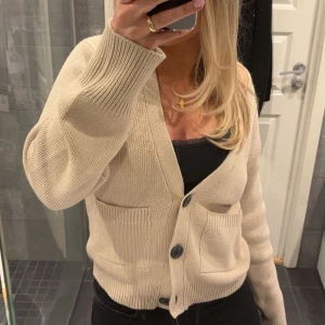 Beige kofta med knappar - Säljer en stilren beige kofta med knappar framtill. Koftan har långa ärmar och två praktiska fickor. Perfekt för en avslappnad och bekväm stil. Passar bra till både jeans och kjol.