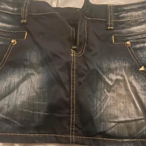 Mörk jeanskjol från Bright Blue - Snygg mörk jeanskjol med slitna detaljer och dekorativa nitar. Kjolen har flera fickor och en cool logga baktill. Perfekt för en avslappnad stil med en edgy touch. Storlek 36 men funkar på mig som har storlek 34.
