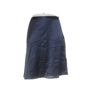 Mörkblå kjol från Busnel - Elegant mörkblå kjol från Busnel i ett glansigt material. Kjolen har en klassisk A-linjeform och en diskret dragkedja i sidan. Perfekt för en stilren look.