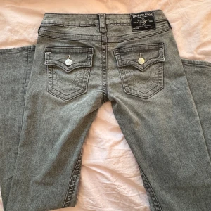 True Religion Jeans - Gråa jeans ifrån true religion med låg midja i modellen Joey, med vida ben. Byxorna har klassiska femficksdetaljer och knappar fram. Byxorna är i nyskick och är använda 1 gång. Fråga om du vill veta mer ✨