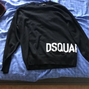 Svart tröja från Dsquared2 - Snygg svart tröja från Dsquared2 med vit textdetalj på framsidan och baksidan. Tröjan har långa ärmar och en klassisk rund halsringning. Perfekt för en stilren look.