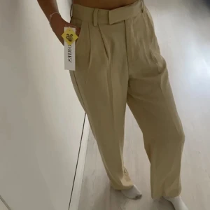 Beige kostymbyxor  - Ett par helt oanvända beige kostymbyxor (prislappkvar) Dessa är endast testade för att ta bilden till försäljning. Jag är 175 o dom passar bra i längden-går hela vägen ner till golvet! Knäpps med dragkedja, knapp och en extra hake-vilket gör midjan är ursnygg! (Liknar madlady’s kostymbyxor) 