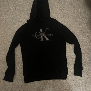 Svart hoodie från Calvin Klein - Snygg svart hoodie från Calvin Klein med deras ikoniska logga på bröstet. Tröjan har långa ärmar och en klassisk huva. Perfekt för en stilren och bekväm look.