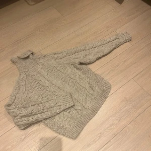 Beige stickad polotröja - Säljer en mysig beige stickad polotröja med flätmönster. Tröjan har långa ärmar och en hög krage som håller dig varm under kyliga dagar. 
