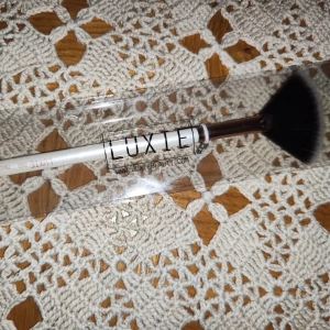 Luxie 560 Medium Fan Brush - Säljer en Luxie 560 Medium Fan Brush med vitt handtag och mjuka, svarta borst. Perfekt för att applicera highlighter eller bronzer med precision. Borsten kommer i en genomskinlig förpackning.