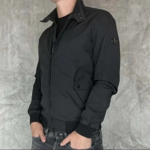 Svart bomberjacka från J. Lindeberg - Snygg svart bomberjacka från J. Lindeberg med dragkedja och ribbade muddar. Jackan har en stilren design med en diskret logotyp på ärmen. Perfekt för en cool och avslappnad stil. Skicket är 10/10 kom med frågor, passar mig som är 178cm men rekommenderar inte för längre personer, nytt pris 3500 mitt pris 1000