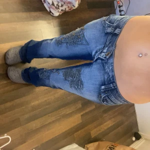 Lågmidjade jeans  -  coola jeans som är lågmidjade med unika slitningar och nitar på framsidan även snygga detaljer på bakfickorna 🎉Mått: 34cm midjemått, 17cm grenhöjd, 75cm i innerbenlängen, 90cm ytterbenens längden. 🥰lite slitna längst ner på baksidan   Vid fötterna❤️