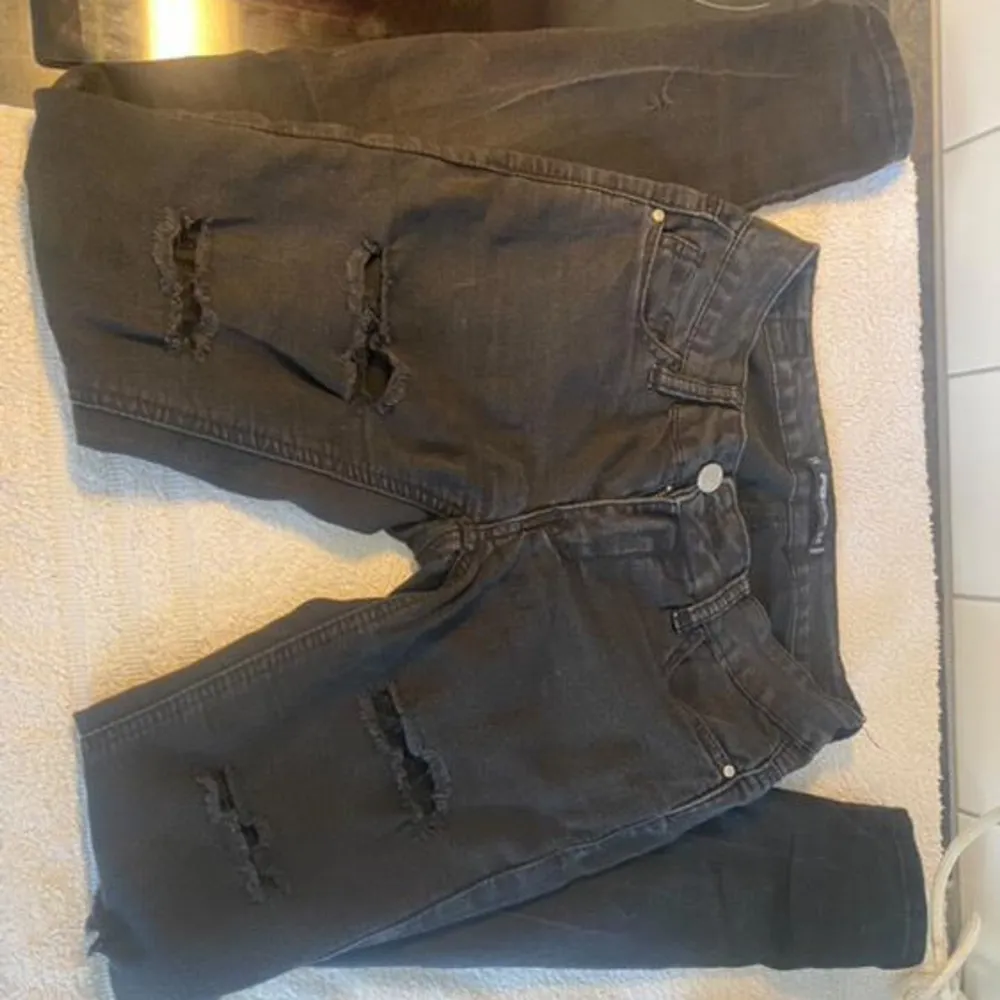 Säljer ett par svarta jeans med coola slitningar på framsidan. De har en klassisk femficksdesign och knappgylf. Perfekta för en avslappnad och trendig look. Passar bra till både vardag och fest! De är lågmidjade och har spetts i hålen. Jeans & Byxor.