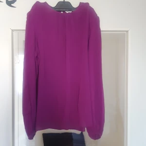 Lila långärmad blus - Säljer en snygg lila blus med långa ärmar. Blusen har en enkel design med en knappdetalj vid ärmslutet. Perfekt för både vardag och fest!