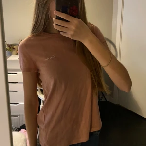 Corallfärgad t-shirt  - T-shirt av bomull, använt ett fåtal gånger, corallfärgad/rosa liknande färg, det står ”love” med små bokstäver på en sida 