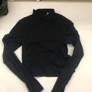 Svart långärmad polotröja - Säljer en stilren svart polotröja med långa ärmar. Perfekt för höst och vinter, den är både bekväm och snygg. Tröjan är croppad vilket ger en modern touch. Passar bra till både vardag och fest!