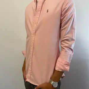 Säljer en snygg rosa oxfordskjorta skjorta från Ralph Lauren, slim fit. Långa ärmar och klassiska knappar framtill. Inga fläckar eller defekter, den är i perfekt skick. ORG. Pris ligger på 1495, du för den för endast 600.