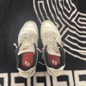 Vita Nike Air Max sneakers - Säljer ett par vita Nike Air Max sneakers med röda detaljer och svart insida. Skorna har en synlig Air Max-dämpning i sulan och klassisk snörning. De är i välanvänt skick men fortfarande bekväma och stiliga för vardagsbruk.