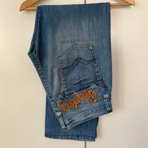 Blå Replay Jeans - Vintage replay jeans med orange brodering över baksidan. Köpta i Milano och har inte sett ett par likadana
