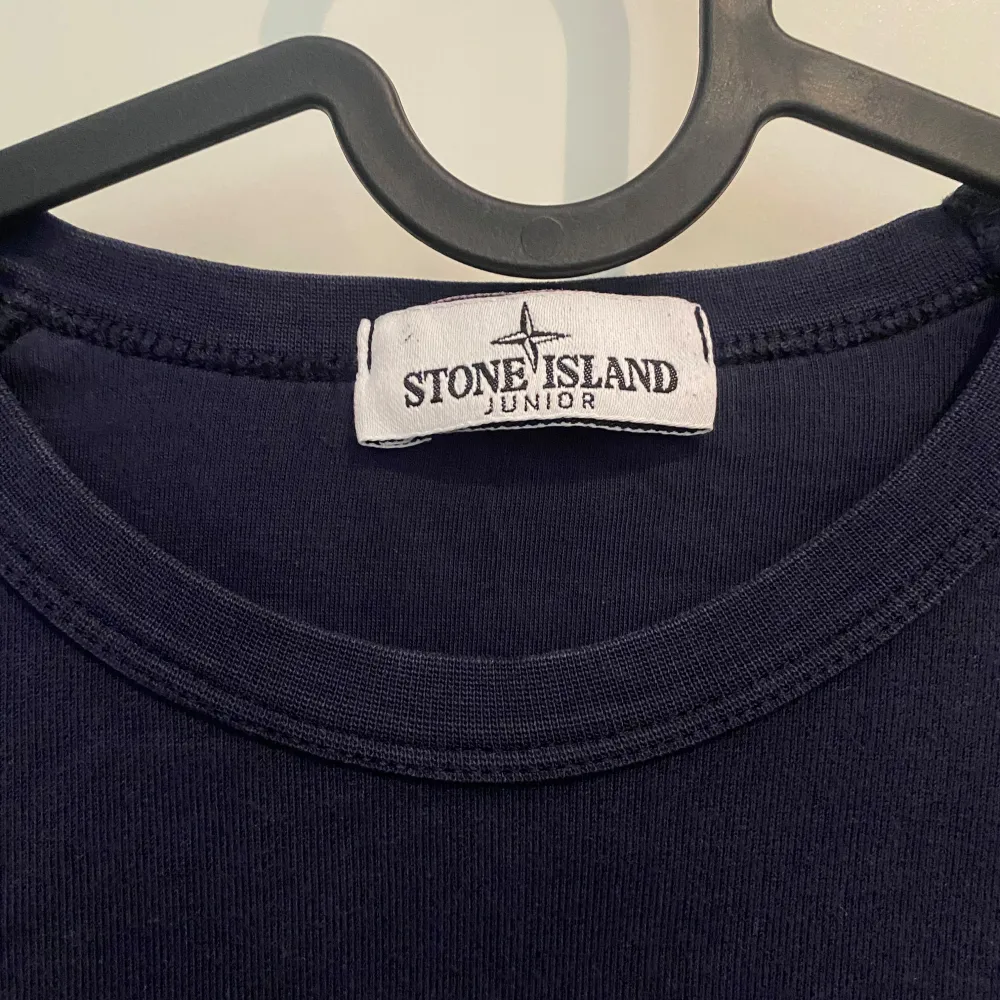 Säljer en snygg mörkblå tröja från Stone Island Junior. Den har långa ärmar och en klassisk rund halsringning. Tröjan är i bra skick och har  Stone Island-märket på ärmen. Perfekt för både vardag och lite mer avslappnade tillfällen. Köpt för 1699.. Tröjor & Koftor.