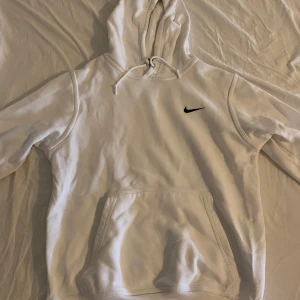 Vit hoodie från Nike - Säljer en klassisk vit hoodie från Nike. Den har en känguruficka framtill och en liten svart Nike-logga på bröstet. Perfekt för en avslappnad stil eller träning. Superbekväm och stilren!