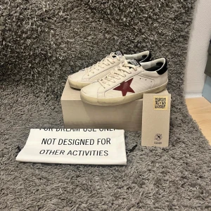 Golden goose  - Ett bar riktigt feta Golden goose sneakers i färg vitt med en vinröd stjärna, storlek 42. Skick är 10/10 då dom är sprillans nya. Box, passport och dustbag medföljer. Hör av dig om du har några frågor. Nypris cirka 6200kr. PRIS KAN DISKUTERAS