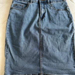 Jeanskjol från Vero Moda - Säljer en snygg jeanskjol från Vero Moda i storlek S. Kjolen har en klassisk blå denimfärg och är i en normal passform. Den har både fram- och bakfickor samt en slits baktill för extra rörelsefrihet. Perfekt för en avslappnad vardagslook!