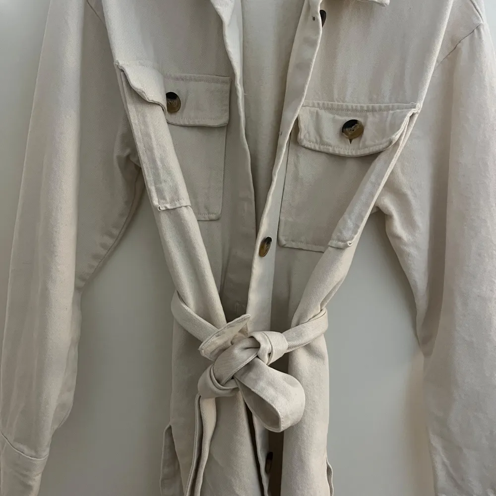 Säljer en superfin beige overshirt från Bik Bok i storlek XS. Den har långa ärmar och knappar framtill, samt två stora fickor på bröstet. Materialet känns som bomull och den har ett bälte i midjan för en snygg passform. Perfekt nu till höst!. Takit.