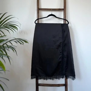 Kjol - Högmidjade knälång kjol med slits på sidan. Materialet är silk 