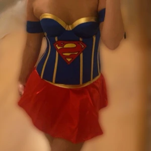 Superwoman utklädnad  - En kostym i två delar, Blå korsett med guld detaljer samt röda märket, vadderade kupor så man behöver ingen Bh. Och en röd kjol med resårband. Fint skick inga fläckar eller skador😍